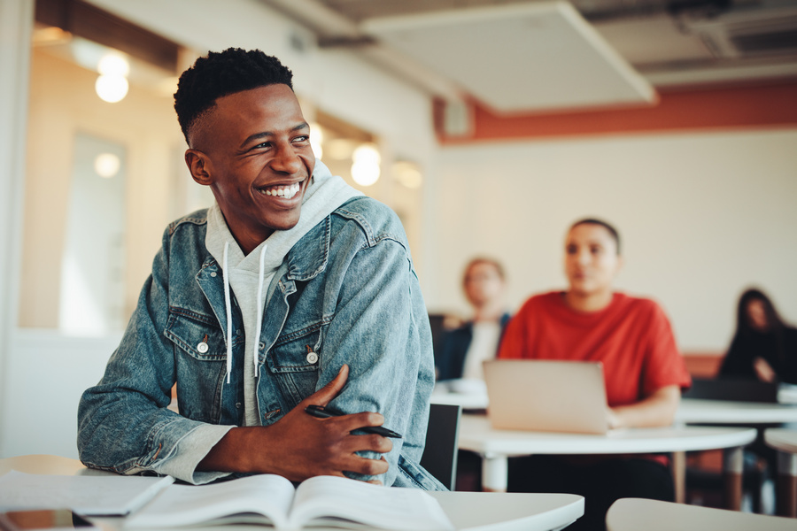 Male student sitting in university classroom looking away and smiling. Man sitting in lecture in high school classroom.