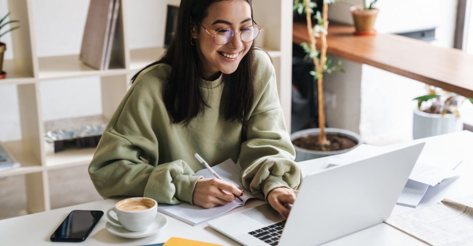 Image of a pretty positive optimistic young girl student using laptop computer indoors studying.