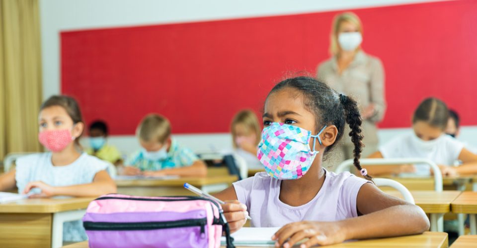 Diligent african tween girl in protective mask studying in school with classmates. New life reality in coronavirus pandemic