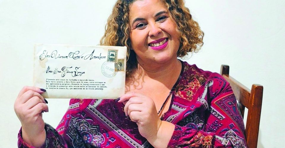 A escritora Tânia Souza posa com sua obra inspirada em cartas e selos antigos - Foto: reprodução