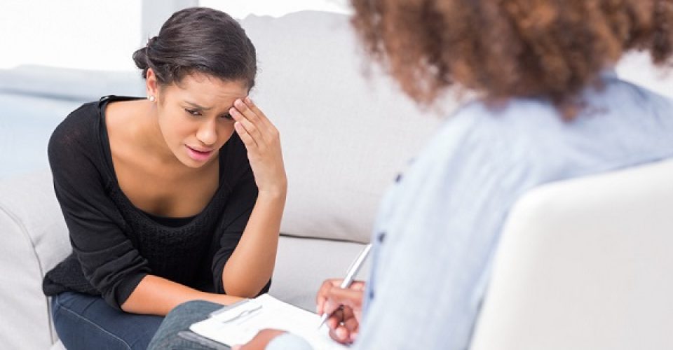 Woman crying on sofa during therapy session while therapist is taking notes